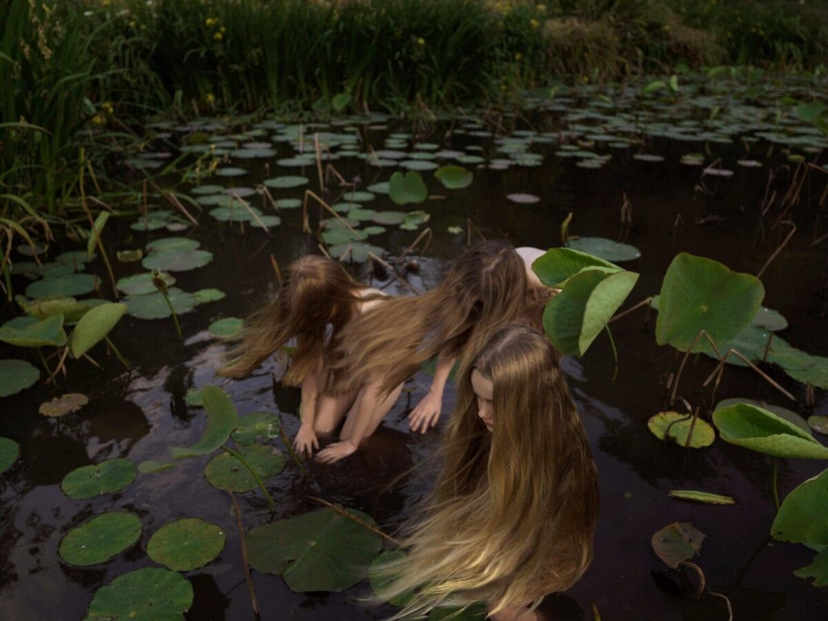 Фотография Тамары Дин: три фигуры с длинными волосами в воде среди листьев кувшинок