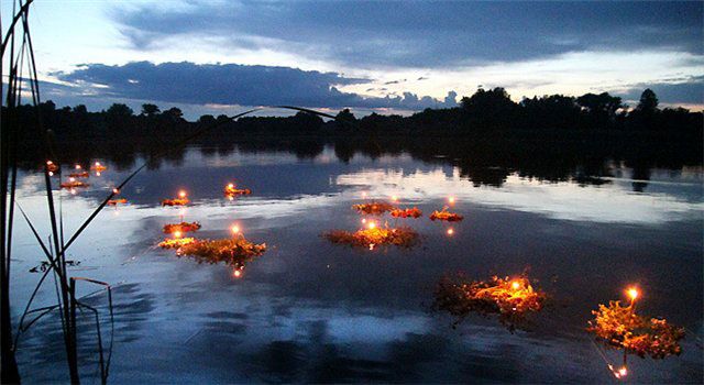 Венок с горящими свечами плывёт по тёмной реке, отражение огня в воде &mdash; купальское гадание