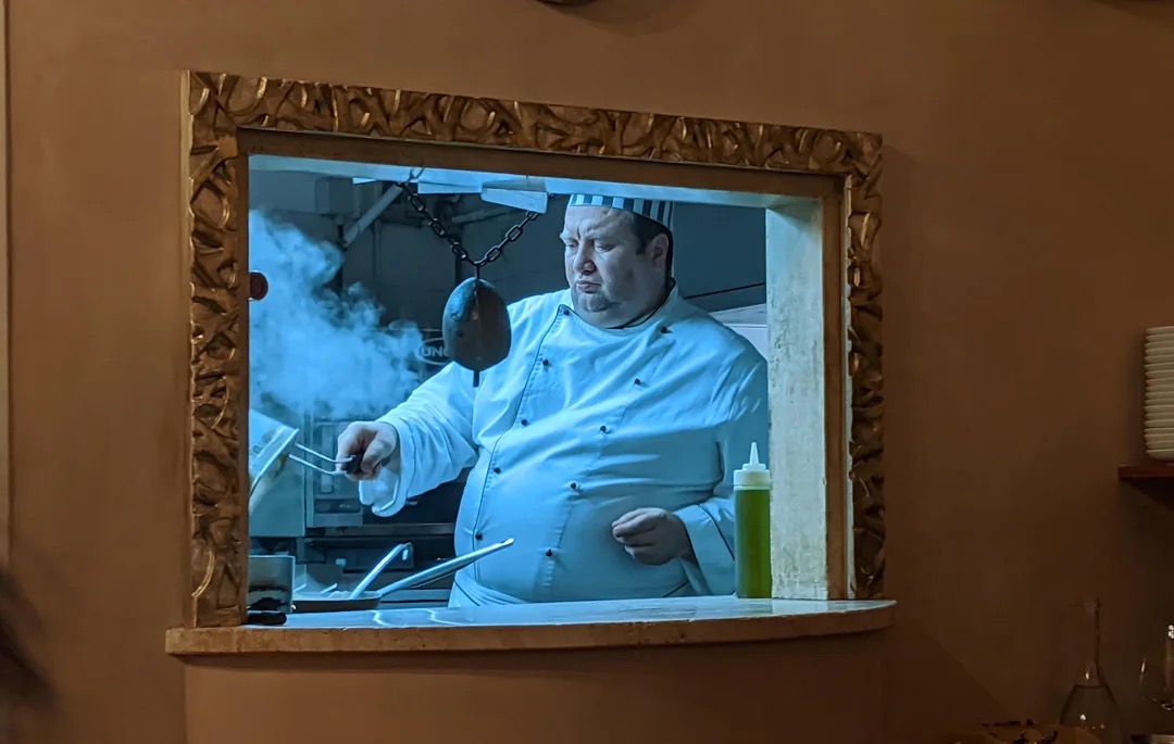 Повар в белом кителе смотрит через окно кухни
