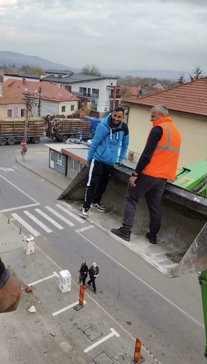 Двое мужчин стоят в ковше погрузчика над улицей города