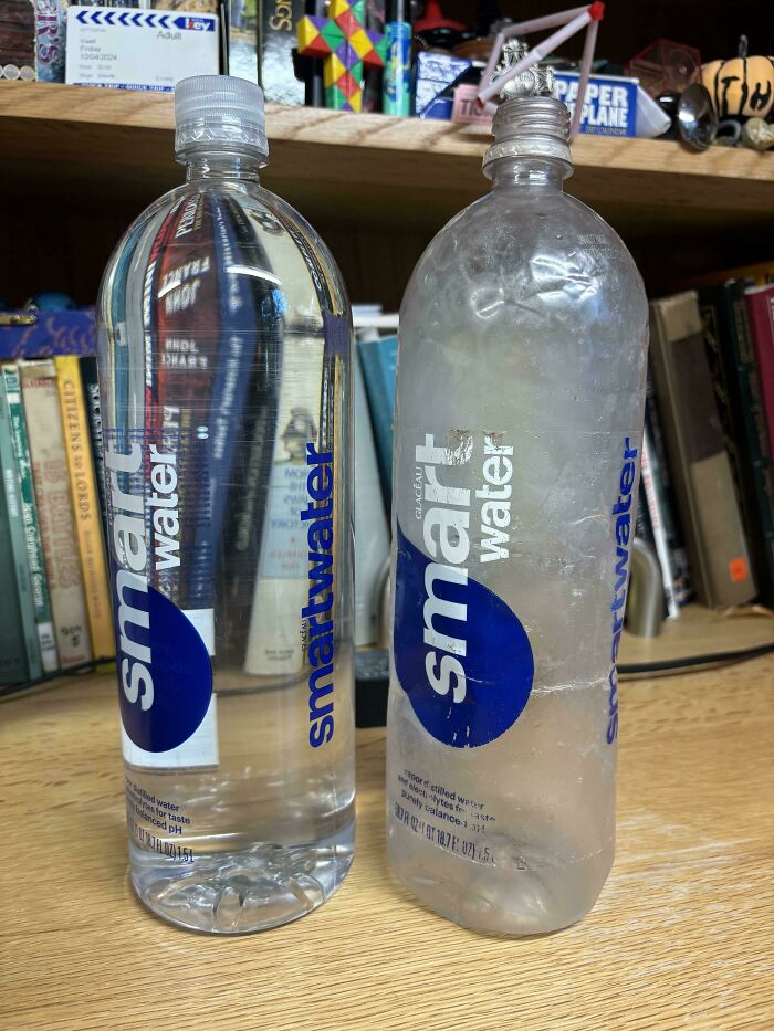 Полная и смятая бутылки Smartwater на столе у книг