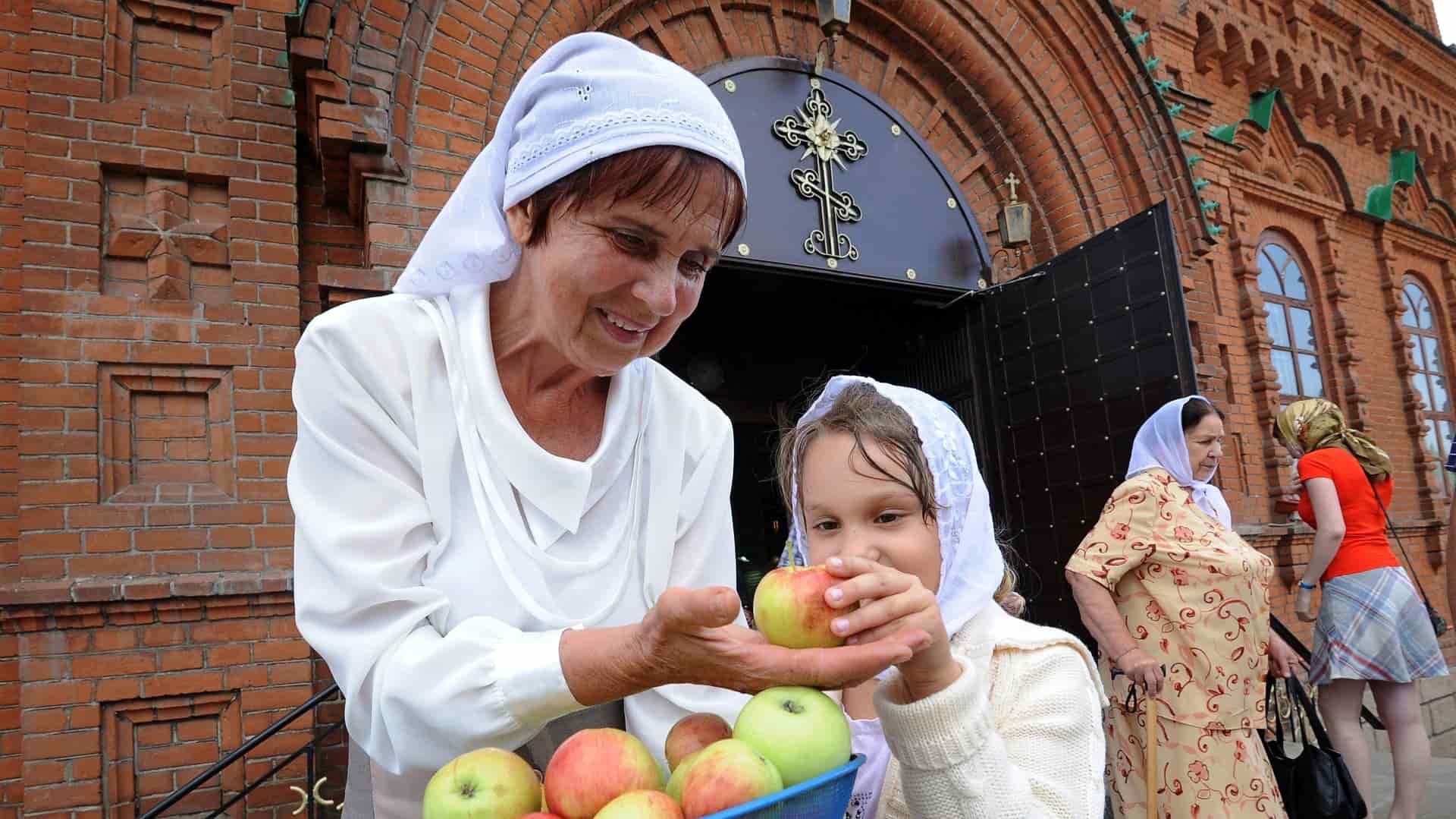 Бабушка и внучка несут яблоки в корзине к храму на освящение