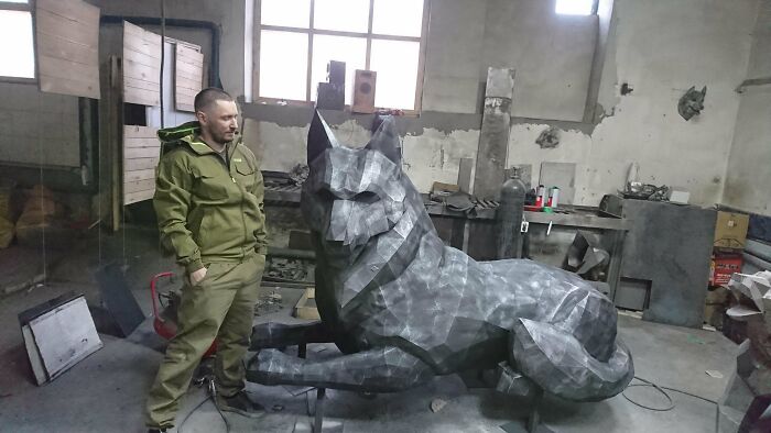 Мужчина в мастерской рядом с лежащим гранёным металлическим волком