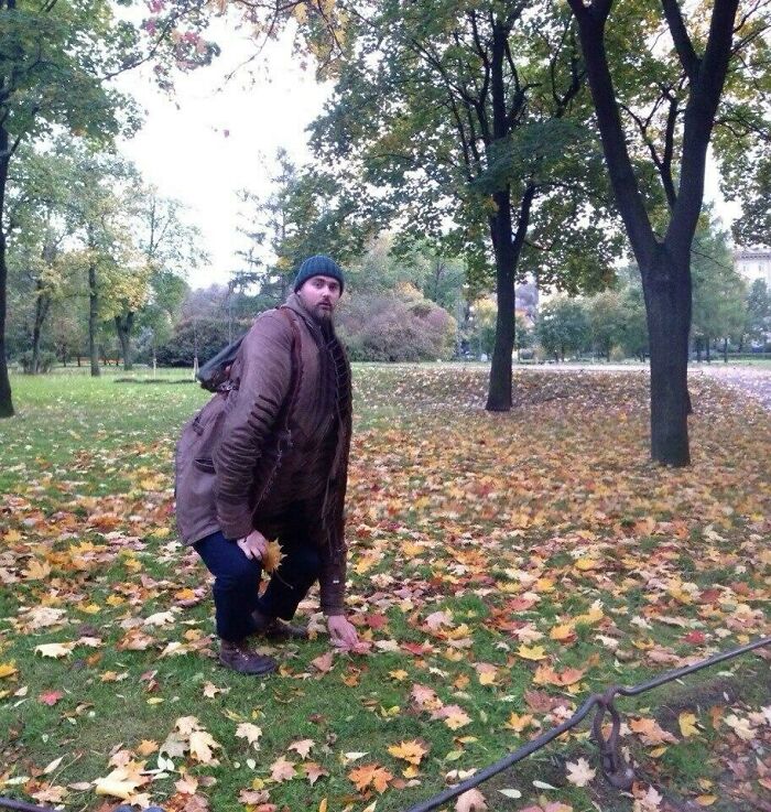 Мужчина в шапке странно согнулся среди осенних листьев