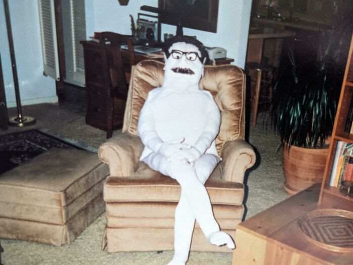 Человек в белом костюме с усами сидит в кресле