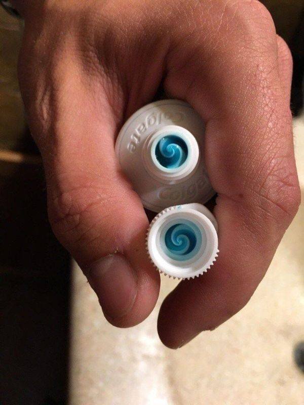 Рука держит две крышки пасты Colgate со спиралью