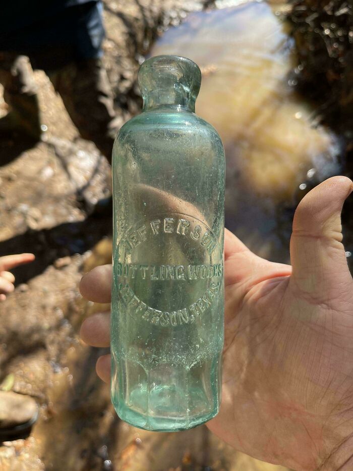 Зеленая бутылка Jefferson в руке у воды