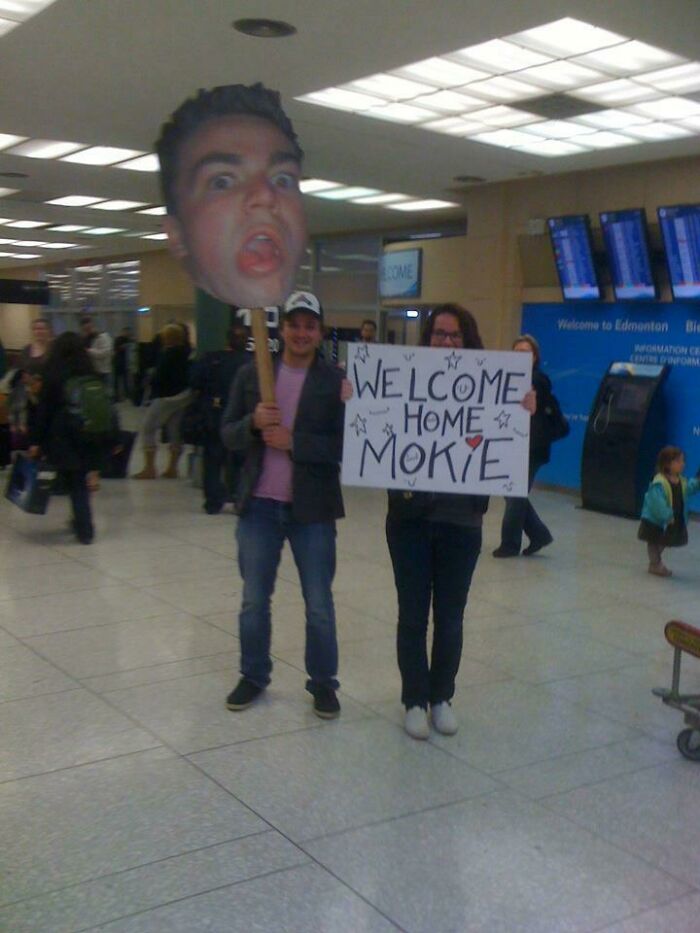 Двое держат огромную картонную голову и плакат WELCOME HOME MOKIE