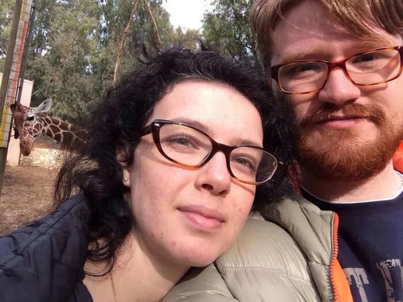 Пара делает селфи в зоопарке, из-за плеча женщины выглядывает голова жирафа