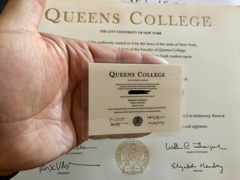 Рука держит мини-диплом Queens College на фоне большого диплома