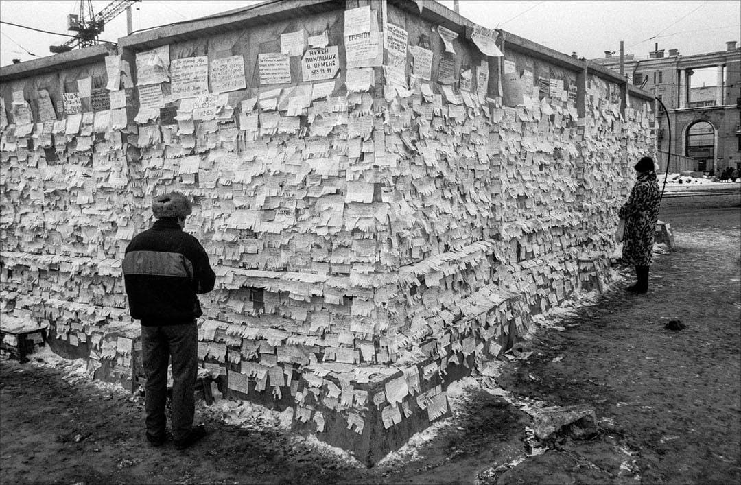 Стена, сплошь заклеенная объявлениями, рядом стоят мужчина и женщина