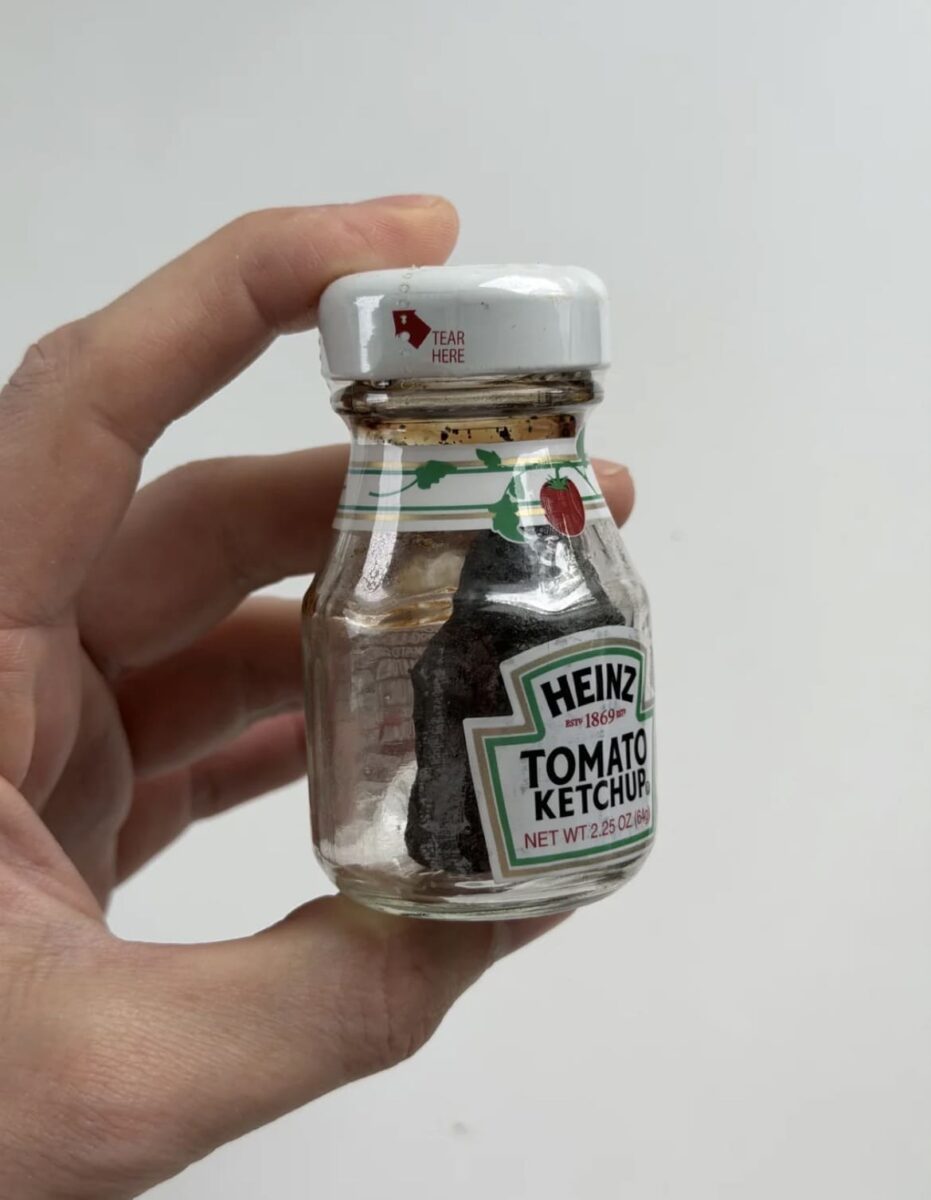 Рука держит банку Heinz с тёмным содержимым и надписью TEAR HERE