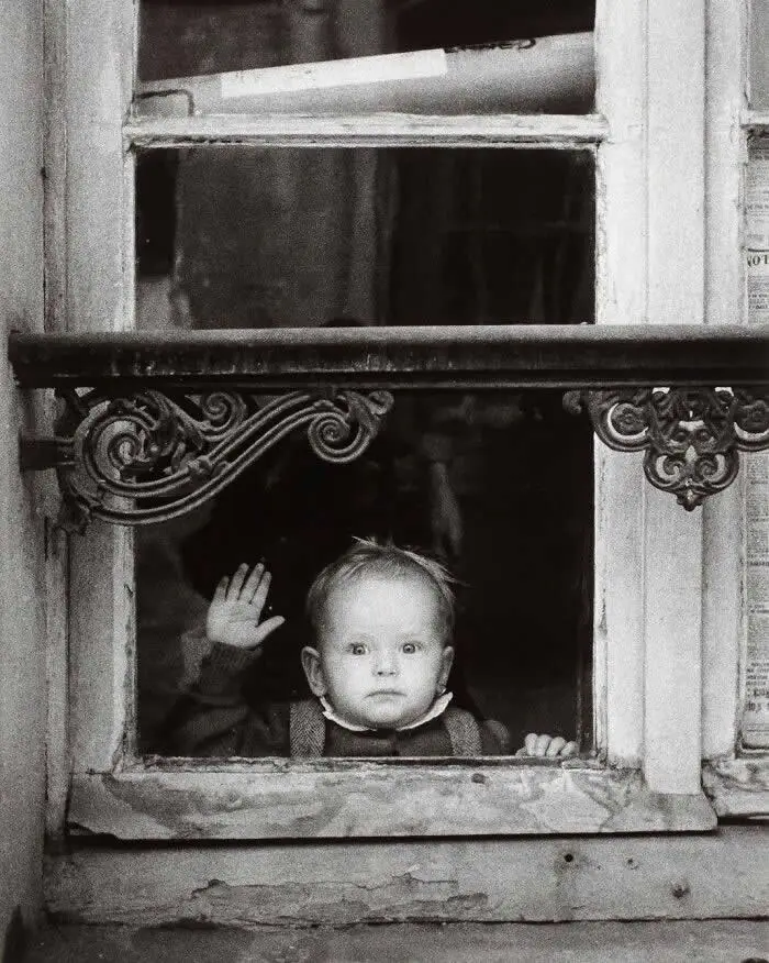 Младенец смотрит в окно с кованой решёткой, поднимает руку. Париж, 1962 год. Фото Кристера Стрёмхольма