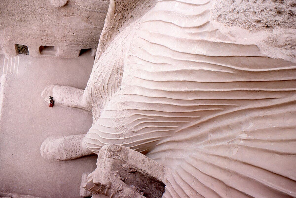 Вид с вершины ниши малого Будды вниз: крошечная фигура человека сидит у подножия, подчеркивая масштаб