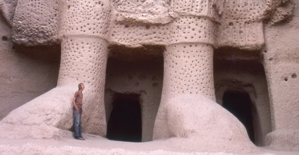 Маленький человек стоит у массивных каменных ступней Бамианской статуи, чтобы показать ее гигантский размер